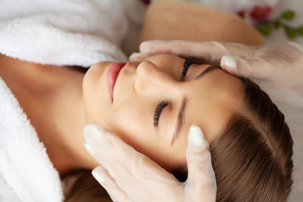 Mujer joven disfrutando del masaje facial en el salón de spa - Foto, Imagen