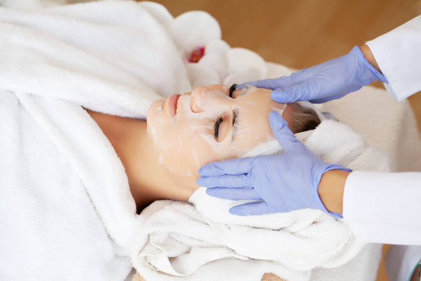 Cuidado de la piel, hermosa mujer con máscara facial en el salón de belleza - Foto, Imagen