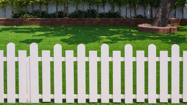Front view of white wooden fence in front of artificial turf with green plant growing on interlocking brick blocks in front yard of home - Photo, Image