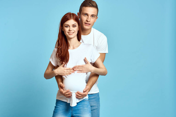 Zwangere vrouw in wit t-shirt en man getrouwd stel wachten op baby blauwe achtergrond bijgesneden weergave van emoties - Foto, afbeelding