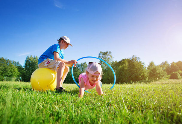 Children are playing on the sport field with hula hoop and rubber fitness ball - Photo, image