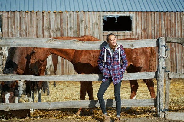 American female breeder standing by stable with horses on countryside farm or ranch. - Fotó, kép
