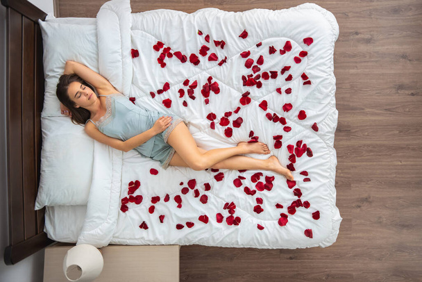 De aantrekkelijke vrouw die op het bed slaapt met een rozenblaadje. zicht van bovenaf - Foto, afbeelding