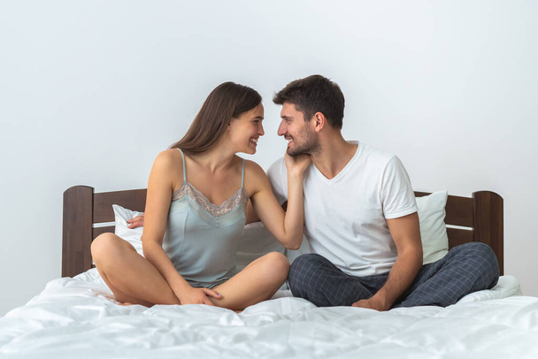 De gelukkige man en een vrouw zitten op het bed op de witte achtergrond - Foto, afbeelding