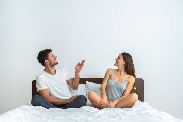 The happy couple sitting on the bed and gesturing - Фото, изображение