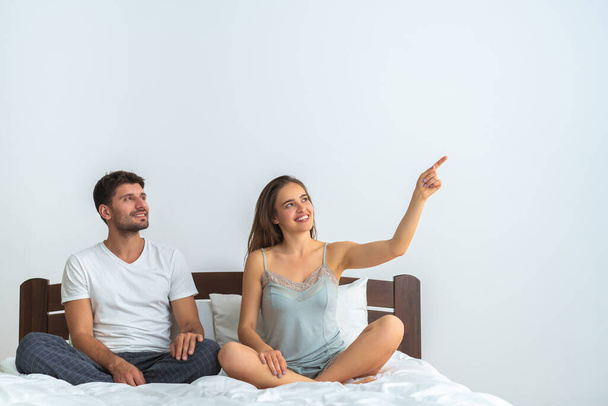 The happy couple sitting on the bed and gesturing on the white background - Photo, Image