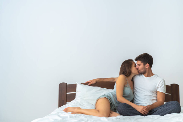 Το ευτυχισμένο ζευγάρι που φιλιέται στο κρεβάτι στο λευκό φόντο - Φωτογραφία, εικόνα