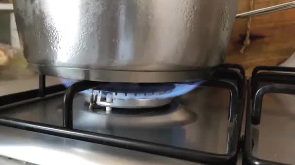Vista ravvicinata della fiamma ardente di una stufa in una cucina domestica che riscalda il contenuto di una pentola d'acciaio. Cucinare a casa. Movimento di panning da sinistra a destra - Filmati, video