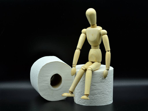 houten etalagepop zittend op een rol toiletpapier - Foto, afbeelding