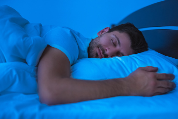 De man die op het bed slaapt. avond nacht tijd - Foto, afbeelding