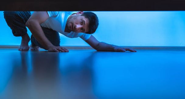 A férfi, aki az ágy alá néz. esti időszámítás - Fotó, kép