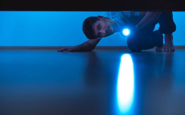The man with a flashlight looking under the bed. evening night time - Foto, imagen