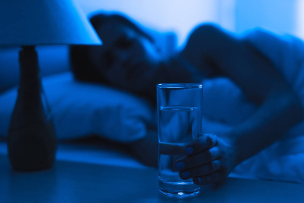 La femme sur le lit tenant un coup d'alcool. soir heure de nuit - Photo, image
