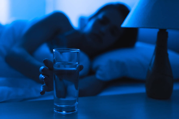 La femme déprimée sur le lit tenant un coup d'alcool. soir heure de nuit - Photo, image