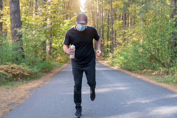 Мужчина в медицинской маске, одежда и кроссовки Nike бегут через осенний лес. Россия, Татарстан, 25 сентября 2020 г. - Фото, изображение