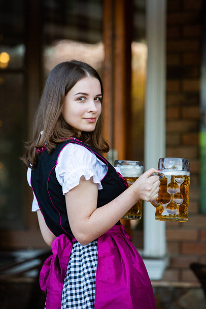 Beautiful Oktoberfest girl wearing a traditional Bavarian dress holding beer mugs. Sexy russian woman in dress with beer. - Photo, Image