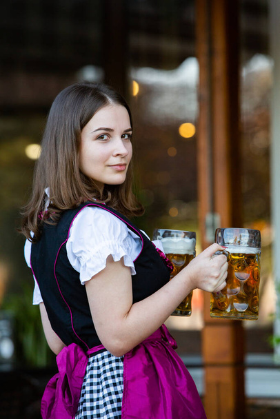 Krásná dívka Oktoberfest na sobě tradiční bavorské šaty držící pivní džbány. Sexy rusky žena v šatech s pivem. - Fotografie, Obrázek