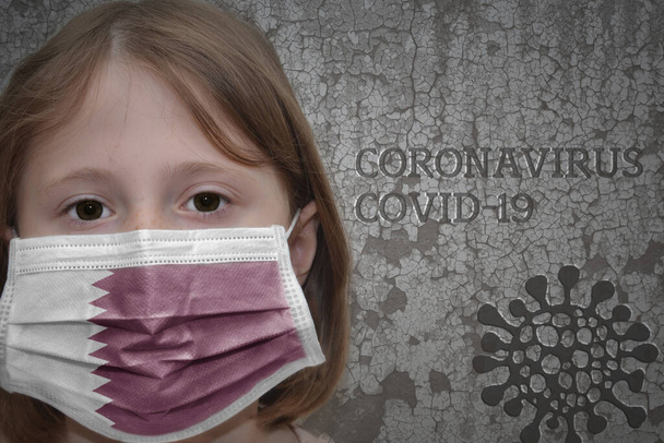 Mała dziewczynka w masce medycznej z flagą Kataru stoi w pobliżu starego zabytkowego muru z tekstowym koronawirusem, covid, i obraz wirusa. Zatrzymać wirusa - Zdjęcie, obraz