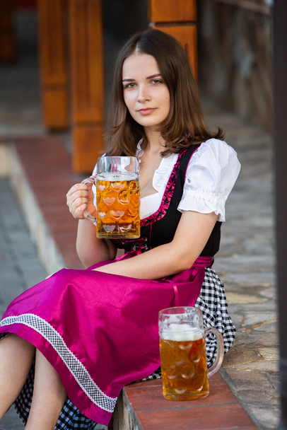Beautiful Oktoberfest girl wearing a traditional Bavarian dress holding beer mugs. Sexy russian woman in dress with beer. - Photo, Image