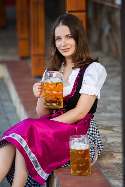 Gyönyörű Oktoberfest lány visel hagyományos bajor ruhát kezében sörös bögrék. Szexi orosz nő ruhában sörrel. - Fotó, kép