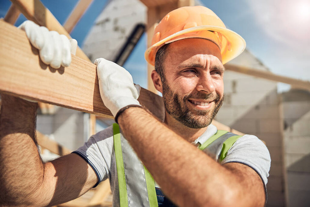 Positive delighted young constructor carrying wooden beam - Photo, Image
