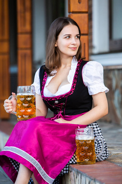 Kaunis Oktoberfest tyttö yllään perinteinen Baijerin mekko tilalla olutmukeja. Seksikäs venäläinen nainen mekko oluella. - Valokuva, kuva