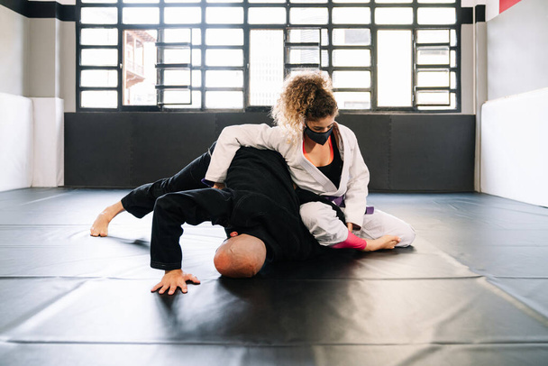 Erkek ve kadın dövüş sanatları eğitimi veriyor ve spor salonunun zemininde kimonolarla judo yapıyor. Yüz maskesi takıyorlar. Çünkü kovid 19 koronavirüs salgını var. - Fotoğraf, Görsel