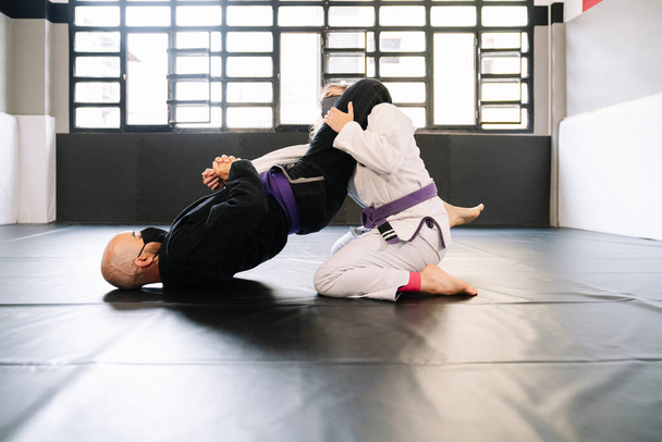 Mies ja nainen harjoittelevat kamppailulajeja ja judoa kimonojen kanssa kuntosalin lattiamatossa kasvonaamiolla 19-koronaviruspandemian vuoksi. - Valokuva, kuva