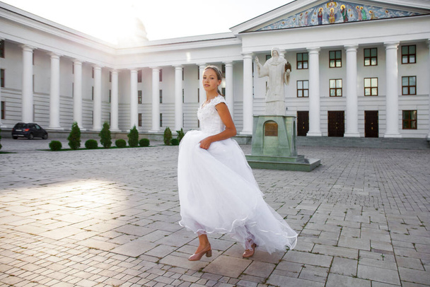 Portrait of a young girl in a white ball gown posing against the background of the Orthodox Cathedral - Photo, Image