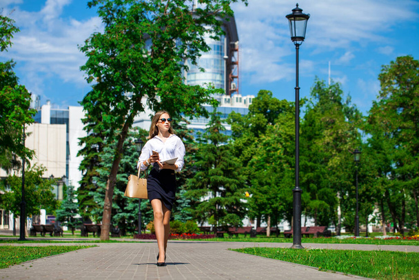 Nuoren liikenaisen muotokuva valkoisessa puserossa ja musta hame kävelee kesäpuistossa, tausta - Valokuva, kuva
