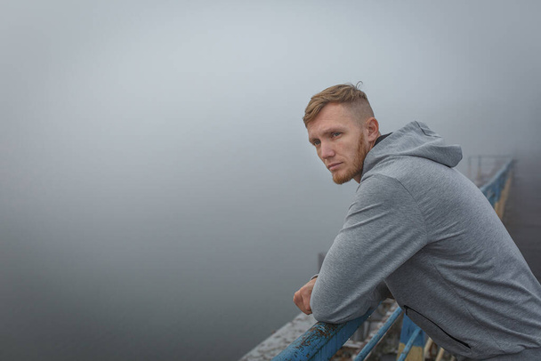 Uomo in felpa grigia rimanere sul ponte in nebbia mattina - Foto, immagini