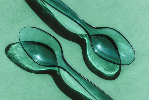 Δύο πράσινα διαφανή πλαστικά κουτάλια με αντίθετες σκιές - Φωτογραφία, εικόνα