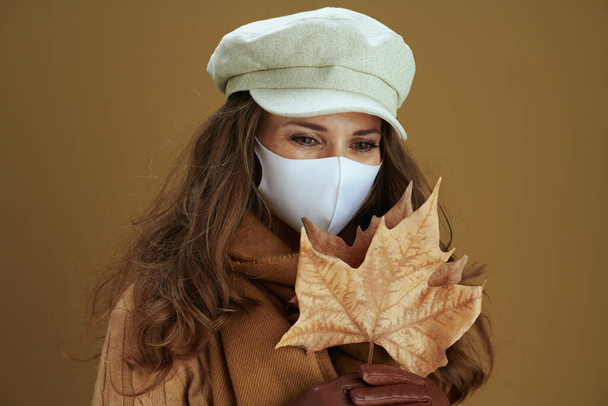 Hello autumn. pensive stylish woman in sweater with white medical mask and yellow autumn maple leaves on beige background. - Фото, изображение