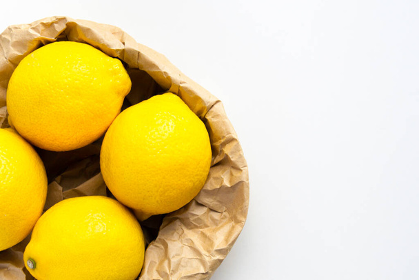 Four ripe lemon on white - grey background. Group of fresh lemon in recycling paper bag. - Foto, Imagen
