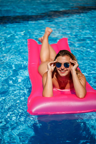 Seksikäs nainen uimapuvussa on vaaleanpunainen puhallettava patja altaassa. Rentoudu uima-altaalla kuumana kesäpäivänä. Lomakäsite - Valokuva, kuva