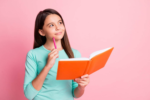 Photo of pretty sweet little clever thoughtful latin lady long hairdo arms hold orange diary pen cheekbone look up empty space wear turquoise sweatshirt isolated pink color background - Φωτογραφία, εικόνα