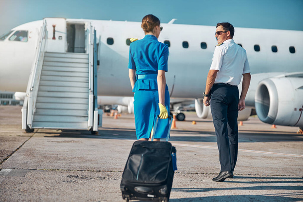 Fröhliche Crew spaziert mit Koffer zum Flugzeug - Foto, Bild