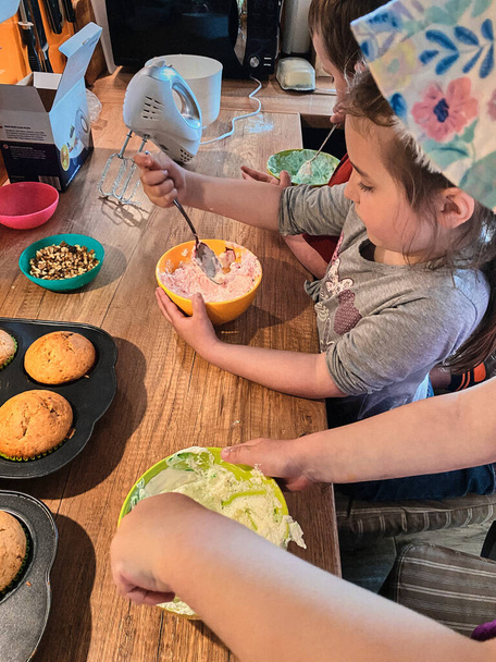 Group of children baking cupcakes, preparing ingredients, toppings, sprinkles for decorating cookies. Kids learning to cook, working together in kitchen at home. Concept of happy family - 写真・画像