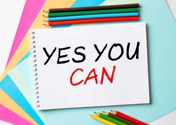 Notatnik z tekstem Yes You Can jest na kolorowym papierze z kredkami. Zdjęcie koncepcyjne - Zdjęcie, obraz