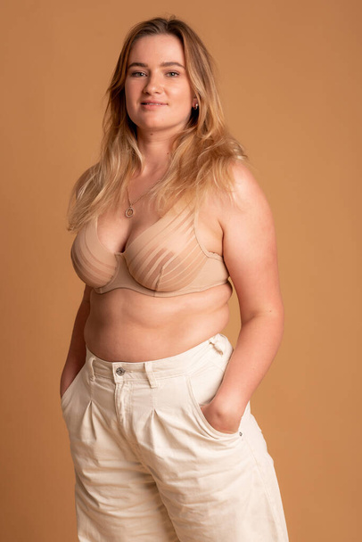 Beautiful overweight woman in beige swimsuit on pink background - Foto, afbeelding