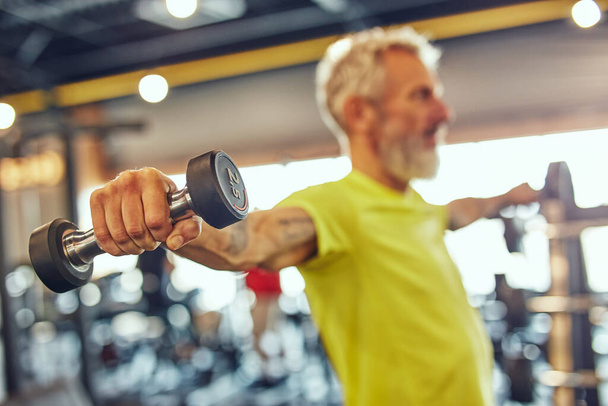 Fit over fifty. Side view of a mature caucasian man exercising with dumbbells at gym, focus on hand - Foto, immagini