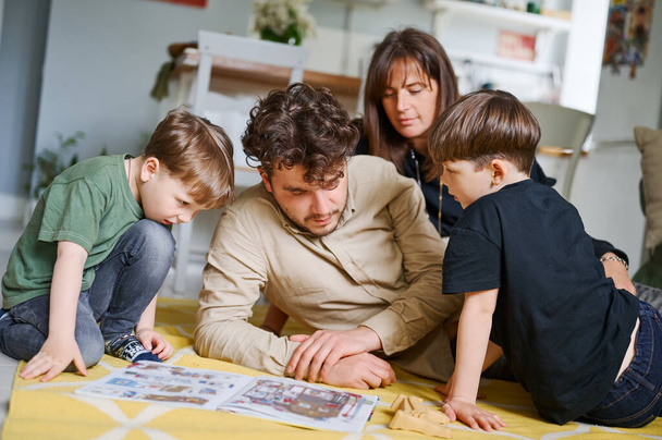 Genç baba evde çocuklarla kitap okuyor. Mutlu aile yerde vakit geçiriyor. - Fotoğraf, Görsel