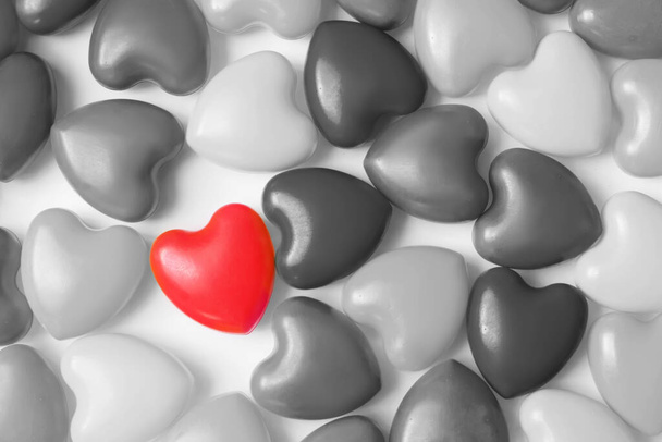 Een rood hart tussen veel zwart-wit harten op witte achtergrond bovenaanzicht. Achtergrond voor Valentijnsdag, verjaardag, vakantie, feest, bruiloft. Harten achtergrond - Foto, afbeelding
