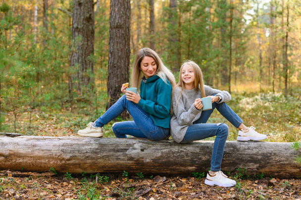 Мама и дочь веселятся, разговаривая в осеннем лесу. Девочки пьют чай на пикнике.. - Фото, изображение