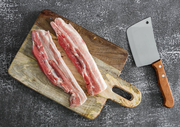 carne y cuchillo Dos pedazos de carne en una tabla de madera y un cuchillo grande se encuentran sobre un fondo de piedra gris, vista superior de cerca. - Foto, Imagen