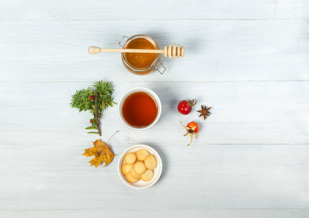 Flatlay with hot tea, a bowl of cookies and honey. On gray boards, with rosehip berries and a dry maple leaf. - Fotoğraf, Görsel