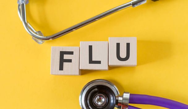 FLU the word is written on wooden cubes lying on a medical background with stethoscope. Concept - Фото, изображение