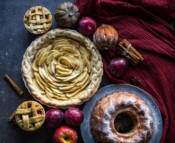 Various apple pies on a table. Top view photo of  classic French apple tart, cake, and small lattice pies. Dark background.  - Fotó, kép
