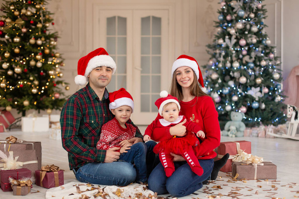 Christmas family. Happy mom,dad and little daughter and son on Santa Claus hat. Enjoying love hugs, holidays people. Christmas tree with garlands in decorated room background. Togetherness concept. - Foto, afbeelding