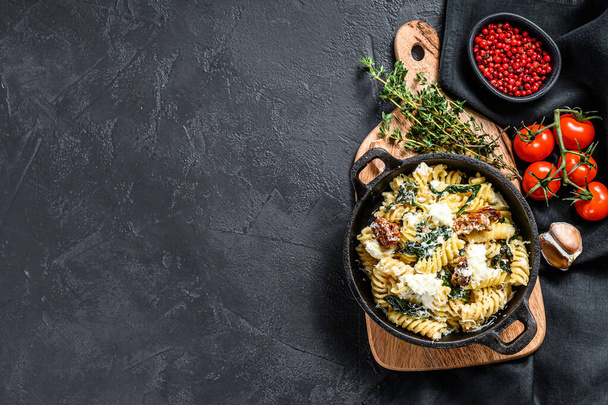 Delicious pasta fusilli dish with creamy spinach sauce and dried tomatoes. Black background. Top view. Copy space. - Photo, Image
